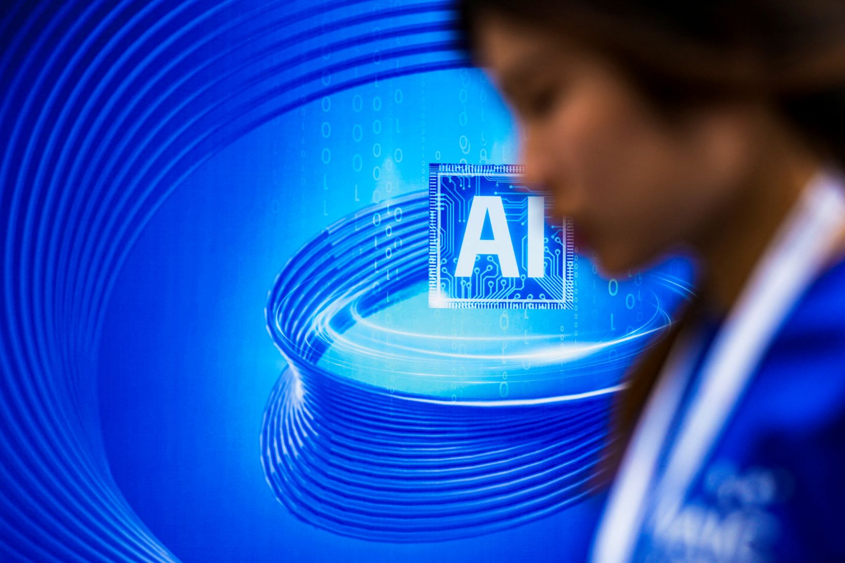 A woman passes in the forefront of an artificial intelligence sign in shades of futuristic blue is seen at the World Artificial Intelligence Conference in Shanghai, China on July 6, 2023. REUTERS/Aly Song