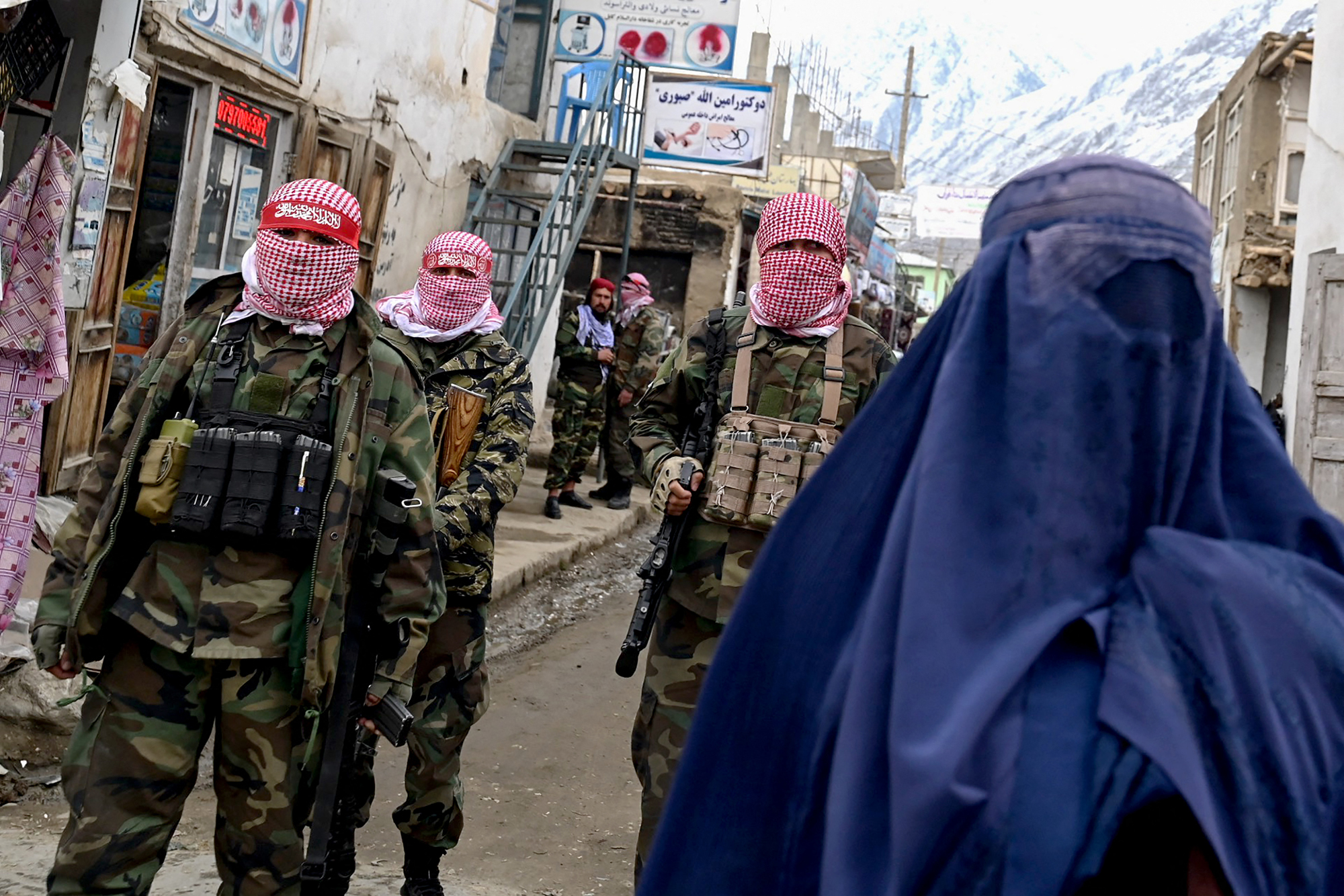 BAHARAK, AFGHANISTAN: Taliban security personnel stand guard as a woman walks along a street at a market in February 2024 in Badakhshan Province.